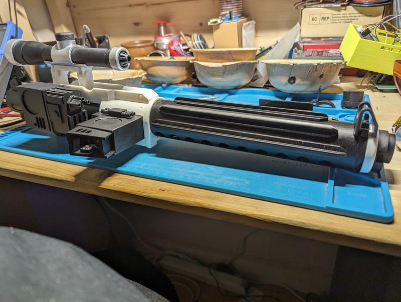 Assembled blaster in black and white resin on a workbench, with a separately mounted scope in black and silver resting above it