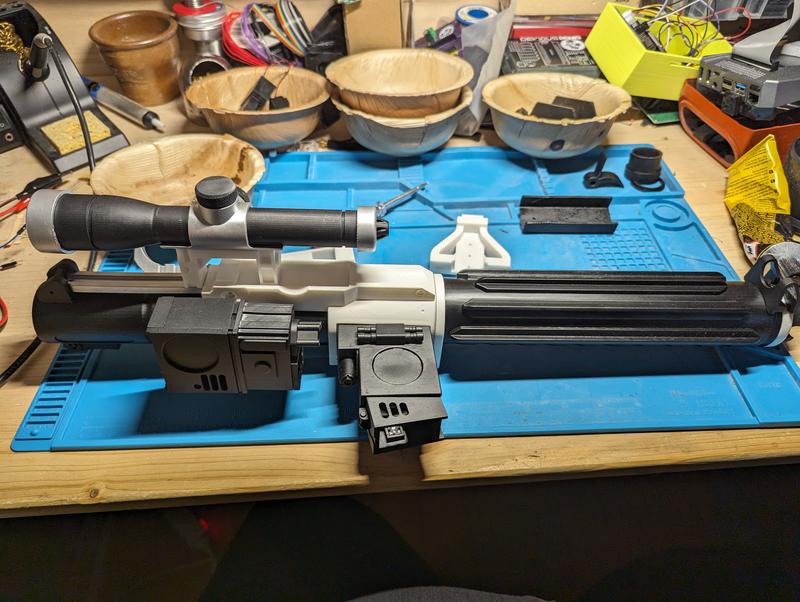 Complete blaster in grey and black resin seen from the side, showing the ribbed barrel shroud, receiver, folding front grip, stock and pistol grip