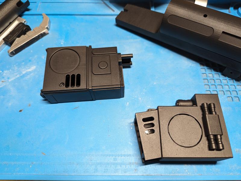 Two black resin greeblie assemblies on a blue mat, each with a circular recess, vent slots and small printed pipe details