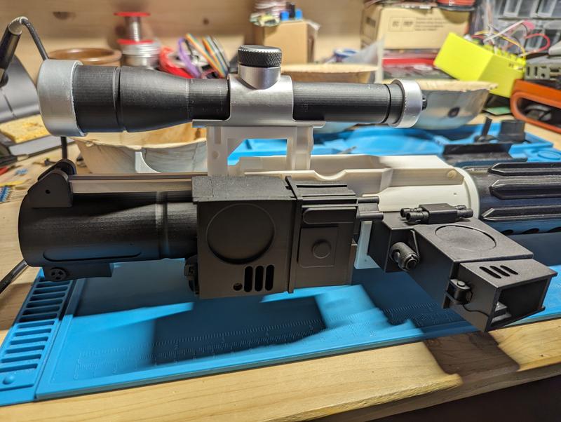 Close-up of the black and silver resin scope with a knurled adjustment knob, mounted on a white printed rail above the blaster body