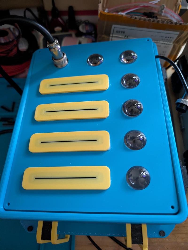 Light blue instrument case seen from above with four yellow raised card slots on the left and six chrome dome-shaped indicator LEDs on the right, connected by a circular aviation connector