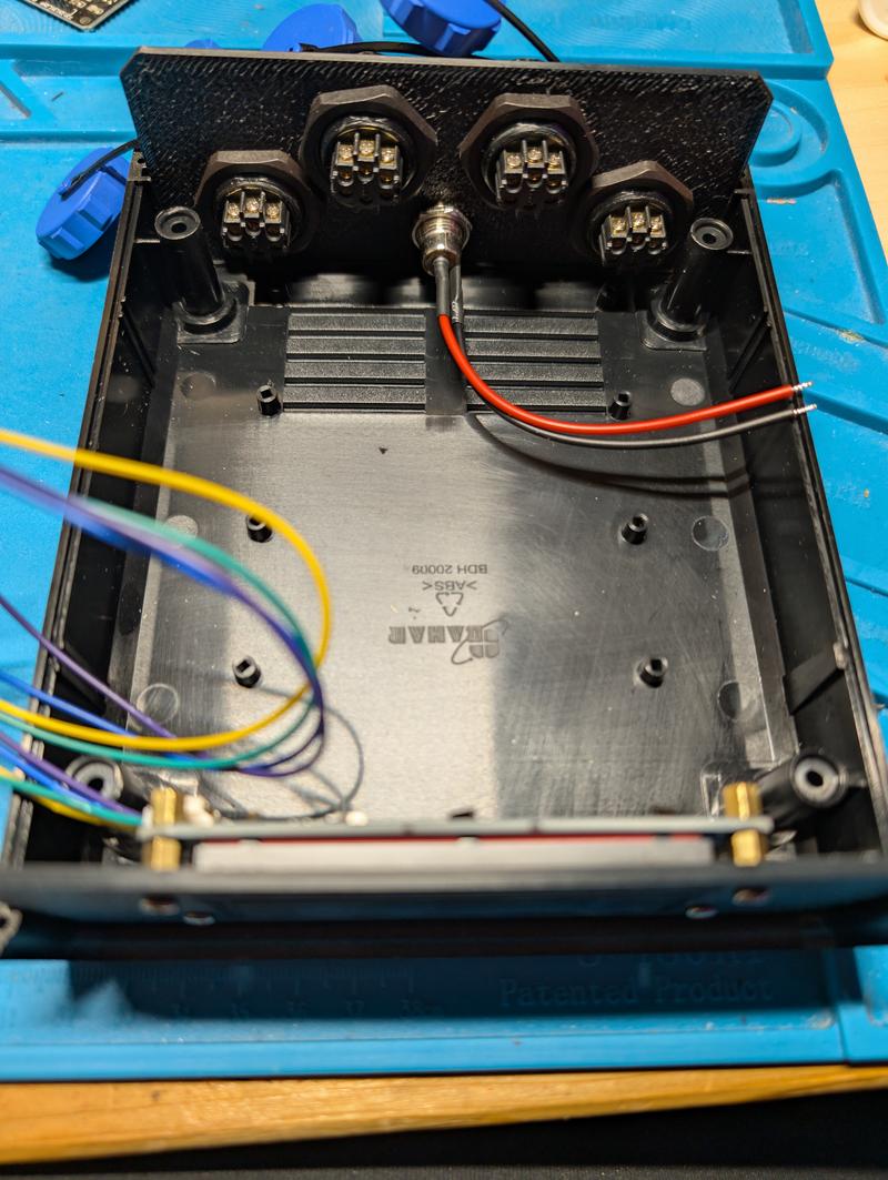 Interior of the control enclosure with the four circular sockets mounted through the end panel, the supply inlet between them and coloured wiring running to the display board