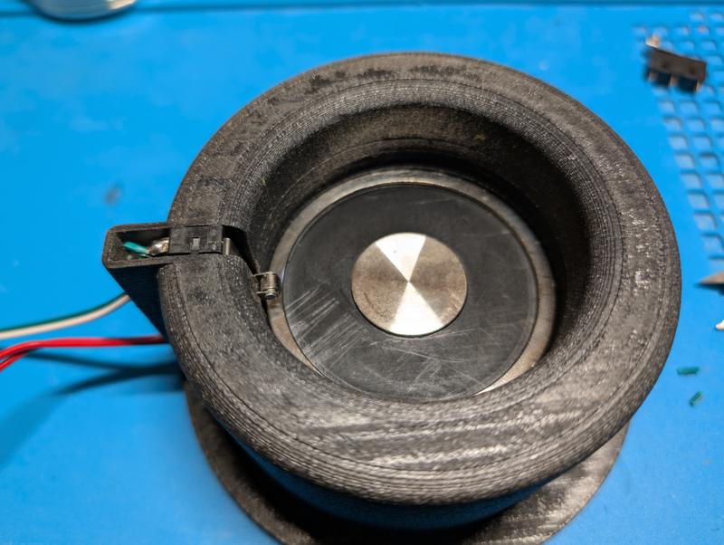 Round black printed housing seen from above with the steel face of an electromagnet inside, a small lever switch mounted at the rim and two wires leaving through a channel in the wall