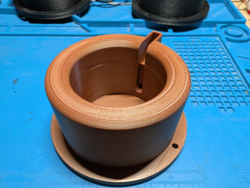 Empty copper-coloured printed housing on a blue mat, showing the internal wall, the cable channel and the mounting flange