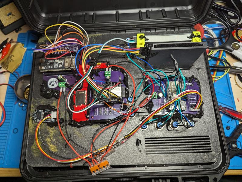 Underside of the panel showing three purple custom carrier boards with ESP32 modules, a red board, screw terminals, lever connectors and dense multicoloured wiring, with hot glue securing the assemblies
