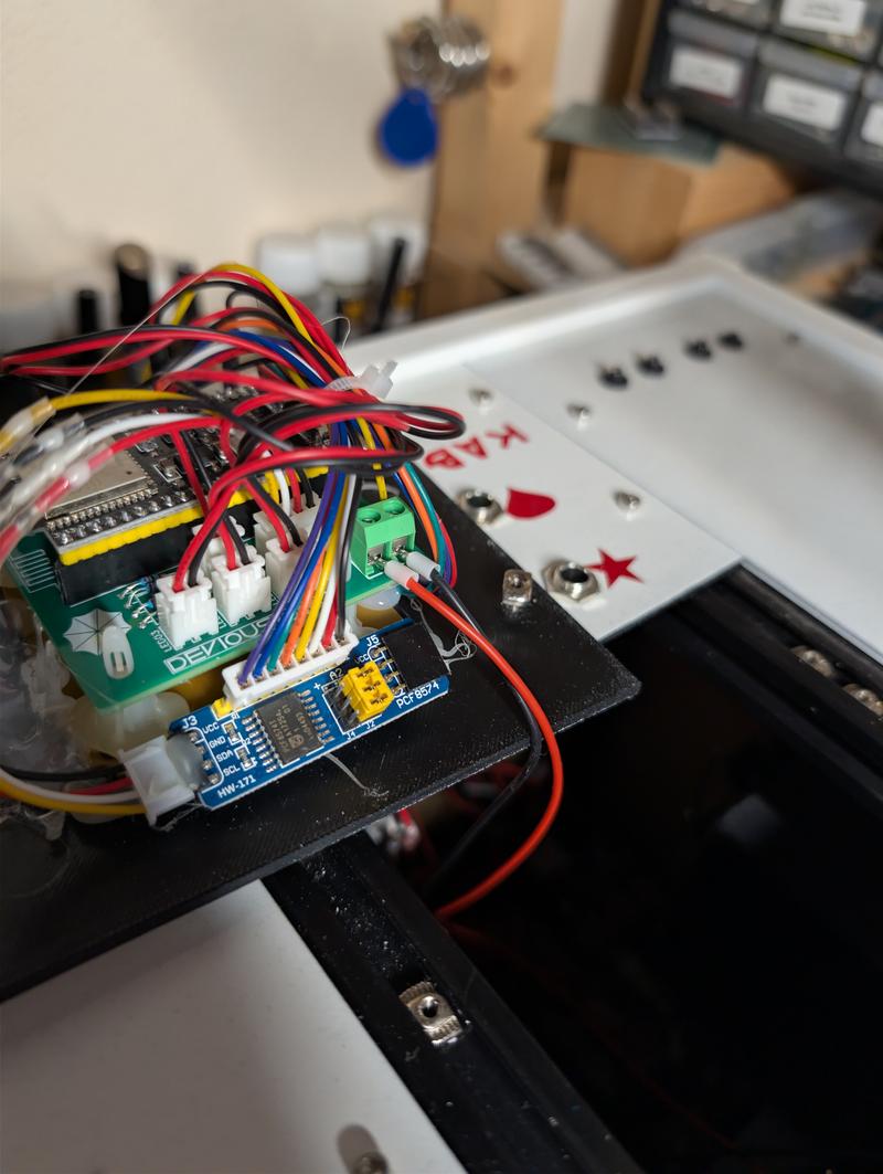 Close-up inside the case: a green Devious City board with an ESP32 and JST connectors, wired to a blue PCF8574 I2C expander module, next to the underside of the cable matrix panel with its sockets and red vinyl markings