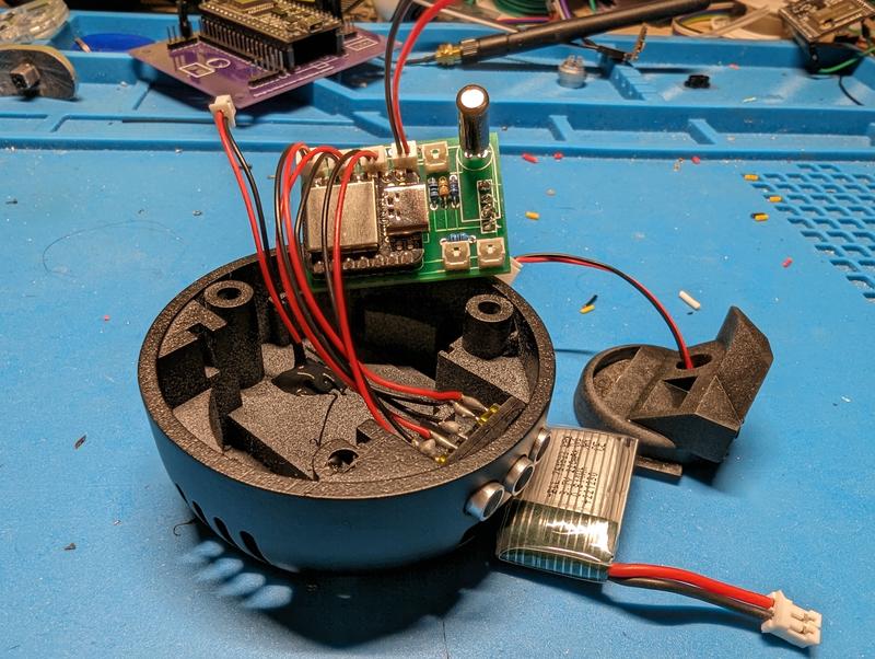 Close-up of the detonator base shell with the green circuit board mounted upright, a Seeeduino XIAO and electrolytic capacitor visible, several red and black JST leads routed into the shell, and a pouch cell lying beside it