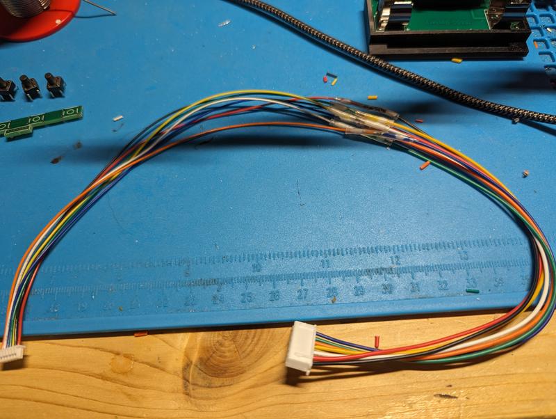 A multicoloured wire harness on a blue mat with a seven-pin JST connector at each end and heat-shrink splices in the middle